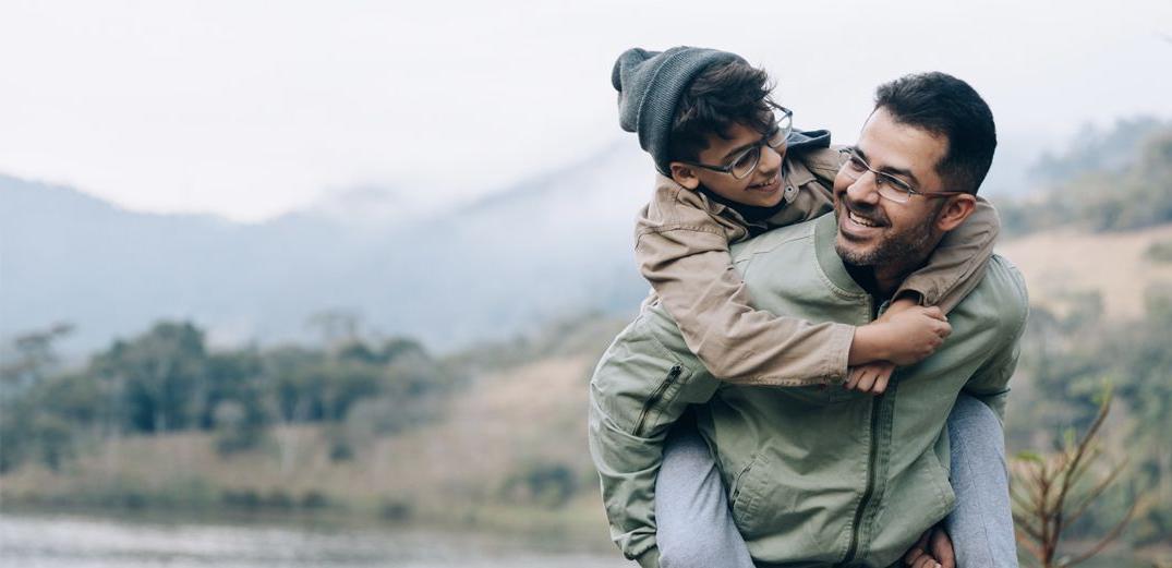 A dad gives his son a piggyback ride on a hike.
