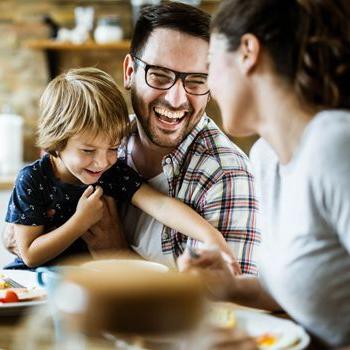 A dad laughs as his child grabs a fork at the dinner table.
